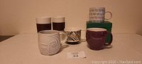 Six Starbucks mugs displayed on flat surface, various colors and designs, one in box.