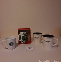 Four Starbucks mugs setup front view, includes boxed floral 2014 mug and three others with Starbucks Coffee text or logo