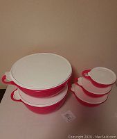Photo showing stacked hot pink Tupperware bowls with white lids of various sizes arranged on a flat surface.