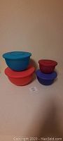 Front view of four Tupperware bowls with lids stacked on countertop. Colors and sizes visible.