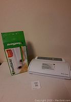 White FoodSaver vacuum sealer machine on table next to its box showing product image and branding
