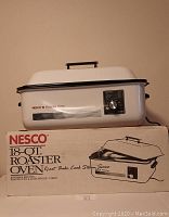 Nesco 18-Quart Roaster Oven sitting on top of original box; white body with black trim and handle, red Nesco logo, control knob on side.