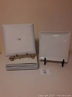 Nine white square dinner plates stacked with two plates on stands showing front and back.