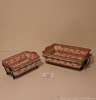 Two Temptations style casserole dishes side by side with matching serving trays and warming stones, photographed from front view.