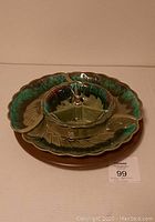 Close-up of vintage green glazed ceramic three-part appetizer serving set with central round dish and metal handle, placed on a brown ceramic base plate.