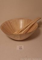 Photo of large wooden salad bowl with wooden salad fork and spoon resting inside, showing bowl shape and wood grain finish