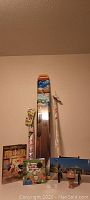 Front view of all items: three kites in packaging standing upright, new panoramic Seattle puzzle in tall box, America states game box, Mickey Mouse book, wooden spinning top