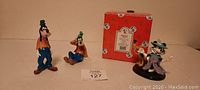 Two Disney Goofy porcelain figurines, one standing and one sitting; Enesco Minnie with Pluto figurine and its original box behind them