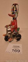 Side view of vintage tin windup duck toy on a tricycle showing colorful details and windup key.