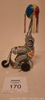 Side angle of vintage tin wind-up elephant on scooter with colorful painted details and tassels on ball.