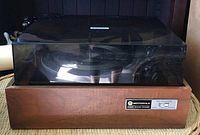 Front view of the turntable with closed clear dust cover and wood casing, showing the overall design and condition.
