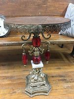 Full side view of vintage side table showing wood top, metal trim, cherub base, and red crystal decorations.