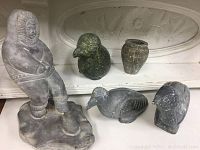 Five Inuit stone sculptures showing one larger figure in parka and four smaller bird and vase pieces arranged in front.