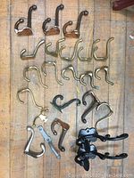 Top-down view of 23 assorted metal hooks laid out on a wood surface showing various finishes and shapes.