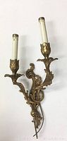 Frontal view of the ornate brass double arm French wall sconce showing detailed leaf decoration and candle-shaped bulb holders with faux wax drips.