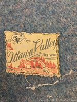 Close-up of Ottawa Valley wool label sewn onto blue side of blanket showing brand name and artwork.