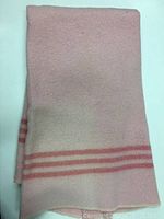 Folded pink and white wool baby blanket, showing pink stripes near edge and overall condition.
