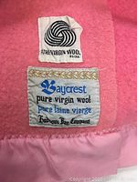 Close-up of wool label indicating pure virgin wool by Baycrest for Hudsons Bay Company sewn onto pink wool blanket.