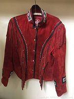 Full front view of a red suede leather jacket with fringe and beadwork details on chest and sleeves, hanging on a hanger.
