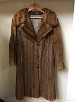 Full front view of the vintage brown fur coat hanging on a wooden hanger showing the overall garment length and shape.