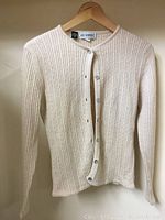 Front view of cream-colored ribbed knit sweater hung on hanger, button-up style.