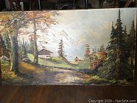 Full view of the vintage oil painting showing landscape with cabins, tall trees, and mountains in the background.