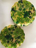 Pair of two round metal trays with scalloped edges, featuring a bright green floral pattern on yellow background