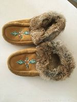 Pair of vintage First Nations moccasins shown from top with visible beadwork on tan suede and fur trim around ankle edges.