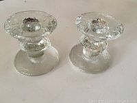 Pair of clear textured glass candle holders with round tops and flat bases, shown side by side.