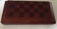 Closed wooden chess board showing checkered pattern on top.