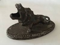 Photo showing the full antique metal lion figurine on an oval base, highlighting paint chipping and wear.