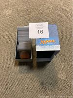 Over 100 Magic the Gathering cards stored inside a metal box with the Coldsnap collector box sleeve beside it on carpet.