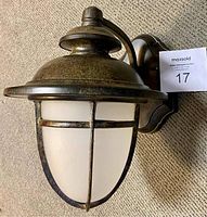 Front angle showing dark rust finish, scalloped wall plate, frosted glass globe with crossbar cage