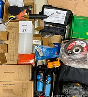 Top view showing test indicator with attached fluid container, stud finders in boxes, cordless drill, grinding disc, and several boxed smaller tools and accessories.