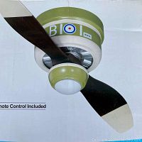 Close-up photo of the ceiling fan showing green and white motor housing with warplane insignia and two dark blades with light tips.
