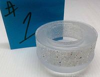 Front-side view of round Swarovski candle holder with textured band of crystals around the middle on a white surface with blue background.