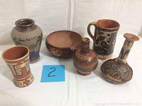 Five pieces of South American pottery arranged on a white backdrop showing variety of shapes and sizes with native designs and reddish hues