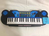 Front view of 37-key portable electric piano with black and blue design, showing keys and speaker areas.