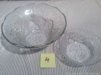 Photo showing the set of two clear glass bowls with fruit and leaf embossed pattern sitting on striped fabric. A marker with the number '4' is visible.