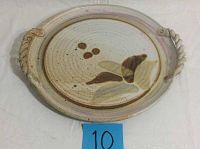 Top-down view of the round handcrafted pottery plate showing the two twisted handles and decorative glaze.