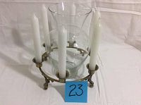 Circular brass candle holder with six white candles and clear glass vase insert, photographed from side angle showing legs and candle holders