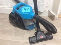 Front angle view of the vacuum showing the dirt container, blue handle, vacuum head and hose setup.