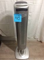 Front view of silver tower fan with top control panel visible.