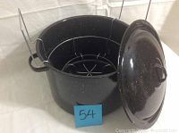 Black enamel cooking pot with metal handles and inner jar rack, lid leaning on pot showing dent on lid's surface