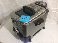 Front and side view of the T-Fal Ultimate EZ Clean Pro deep fryer showing stainless steel body, control panel, lid handle, black side handle, and blue oil filtration outlet.