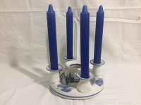 White circular pottery candle holder with blue floral accents holding 4 blue taper candles