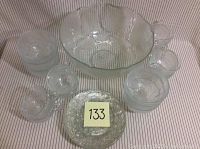 Photo showing entire glassware set including large punch bowl, stack of small bowls, plates, and punch glasses all in clear textured glass.