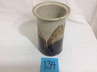 Front and top view of cylindrical pottery vase showing the glazed drip effect in cream and brown shades on dark base.