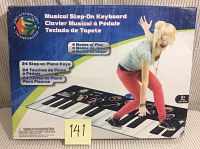 Front of the product box showing a child stepping on the 24 key musical floor keyboard and features in English, French and Spanish.