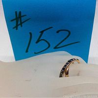 Ring displayed on a white hand-shaped holder with a #152 blue sign in background showing ring shape and partial crystal detail.